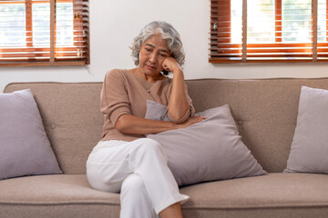 Asian old woman sitting on sofa in living room at home. Lonely, sad, sick and unhealthy with...