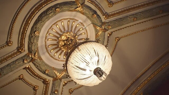 Round crystal chandelier hanging on beautifully decorated ceiling, vintage ceiling lamp decorating royal mansion, palace hall or museum. Antique chandelier illuminating interior design, classic lamps