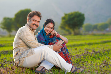 Indian farmer using smartphone with wife at agriculture field.