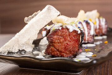 Bocconcini di carne di bufalo, con crema di formaggio, e cialde di riso soffiato serviti su un piatto nero come antipasto in una braceria