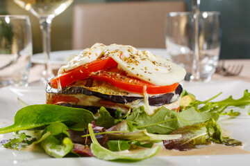 Millefoglie di melanzane con mozzarella filante e pomodori servita in un ristorante elegante come secondo piatto