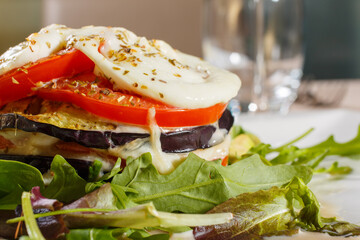 Millefoglie di melanzane con mozzarella filante e pomodori servita in un ristorante elegante come secondo piatto