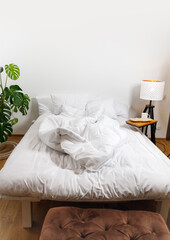 Fototapeta na wymiar Bed with white linens in a minimalist interior with lamp and houseplant and bedside table