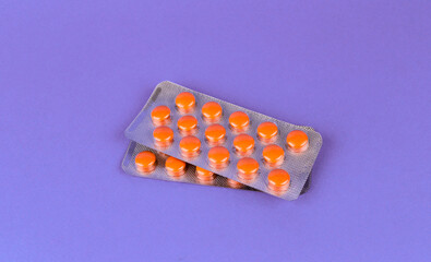 Orange pills in a blister pack on a purple background