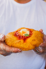 Montanara napoletana appena fritta condita con sugo di pomodoro, mozzarella, basilico e formaggio grattugiato nelle mani con i guanti del pizzaiolo 