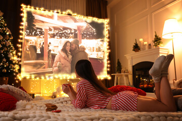 Woman watching romantic Christmas movie via video projector in room. Cozy winter holidays atmosphere