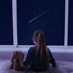 Little girl near window looking at shooting star in beautiful night sky