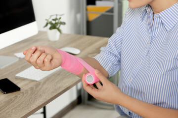 Young woman applying medical bandage onto wrist in office, closeup