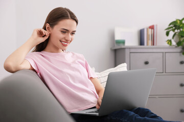 Happy young woman with laptop on sofa at home