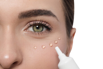 Young woman applying cream under eyes on white background, closeup