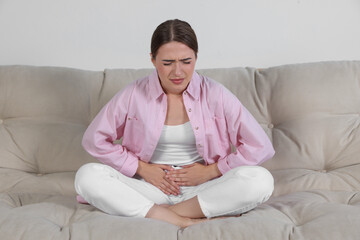 Young woman suffering from cystitis on sofa at home