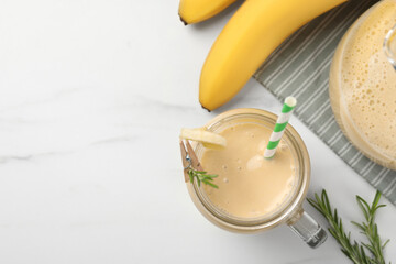 Mason jar of tasty banana smoothie with straw and fresh fruits on white marble table, flat lay. Space for text