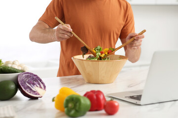 Man making dinner while watching online cooking course via laptop in kitchen, closeup