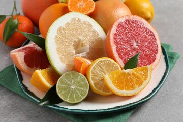 Plate with different citrus fruits and fresh leaves on light grey table, closeup