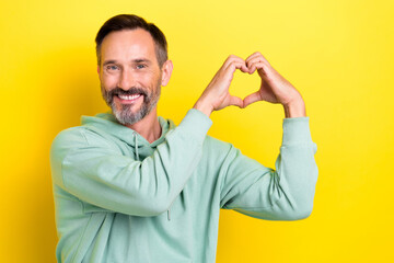 Photo of middle age retired man wear khaki hoodie showing love shape sign enjoy new football club isolated on yellow color background