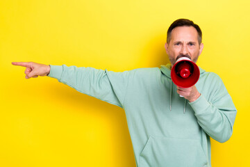 Photo of grey hair angry man businessman wear khaki sweatshirt hold loud speak finger point empty space isolated on yellow color background