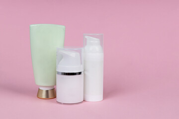 White containers of cosmetics on pink background. Skincare product set. Face and body care concept.