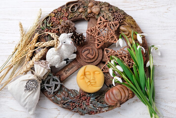 Wiccan altar for Imbolc sabbat. pagan festive ritual. Brigid's cross amulet, sun-moon symbol, wheel of the year, snowdrops, toy lamb on wooden table close up. Imbolc holiday, spring equinox. top view