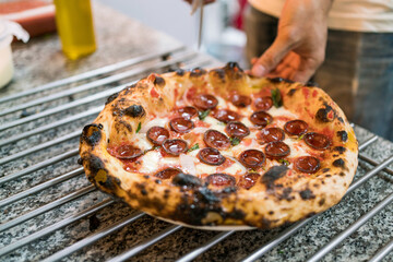Neapolitan pizza style: close-up chef hand cutting chorizo sausage pizza on the pizza cooling rack on the kitchen counter before serving. Italian freshly baked Napoli pizza.