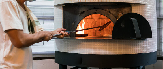 Chef baking Neapolitan pizza in a gas-fired classic Italian pizza oven at high temperature. Crusts...