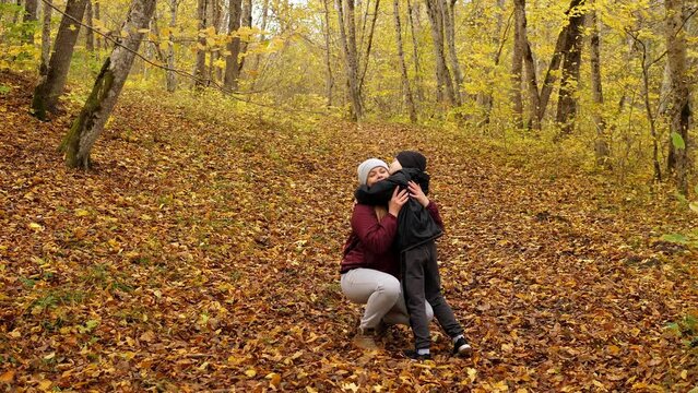 Mother and son in the autumn forest, the boy runs and hugs his mother. A happy family walks in the forest with leaf fall in cool weather.