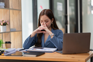 Asian women are stressed while working on laptops, Tired Asian businesswomen with headaches at the office, feeling sick at work, and copy space.