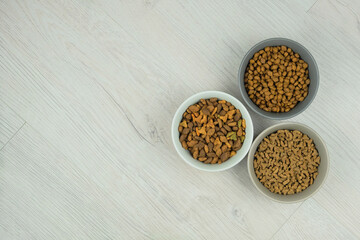 Dry food for cats and dogs in bowls on a white wooden background. Top view. Copy space.