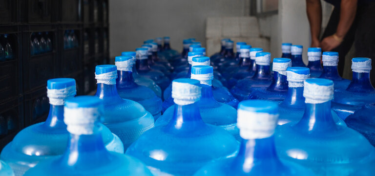 A large number of plastic blue gallons of drinking  water products in a drinking water plant that are arranged in a row waiting to be sold. drink water factory  business concept