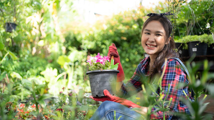 Happy young Asian gardener woman in gloves and apron plants flowers on the flower bed in home...