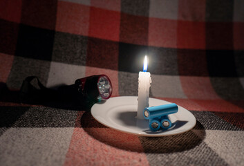 Cylindrical batteries and a headlamp lie near a burning candle (close-up)