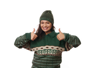 Cheerful African American beautiful woman in warm woolen clothes, smiling a toothy smile and showing thumbs up to the camera, isolated over white background with copy advertising space