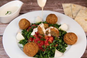 Vegetarian dish, falafel balls from spiced chickpeas with chopped parsley, fresh onions and tomato, tahini sauce, High quality photo