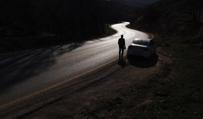 Silhouette of man watching the road ahead. The beginning of a winding, difficult road.  - obrazy, fototapety, plakaty