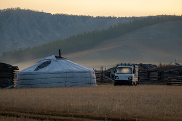 Nomadic yurt in the countryside with the mountains in the background on a sunny evening. Ger tent in the rural country surrounded by forest and hills, car parked next to it.