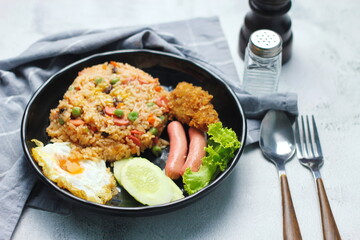 Fried rice with peanuts, carrots, raisins Served with fried chicken, fried egg, and fried sausage. Served on a black plate on a white table in a restaurant.