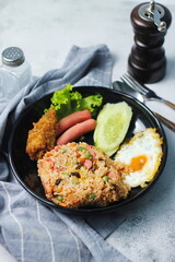 Fried rice with peanuts, carrots, raisins Served with fried chicken, fried egg, and fried sausage. Served on a black plate on a white table in a restaurant.