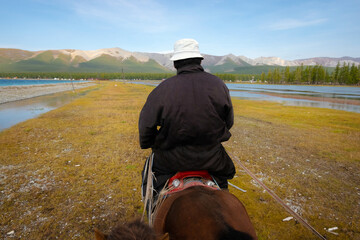 Nomadic man riding horse on the shore of the lake Khövsgöl, blue sky with the clouds in the...