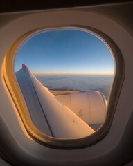 View form an airplane window, blue sky, clouds in the background. Evening sun shining on a planes wing, majestic scenery in the horizon.