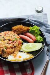 Fried rice with peanuts, carrots, raisins Served with fried chicken, fried egg, and fried sausage. Served on a black plate on a white table in a restaurant.
