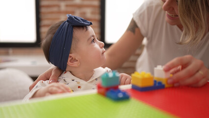 Woman and toddler playing with construction blocks sitting on table at kindergarten