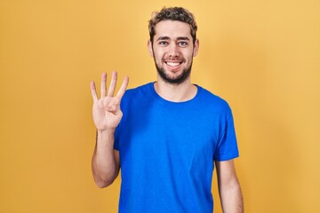 Hispanic man with beard standing over yellow background showing and pointing up with fingers number four while smiling confident and happy.