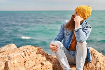 Young redhead man sitting on rock with relaxed expression at seaside