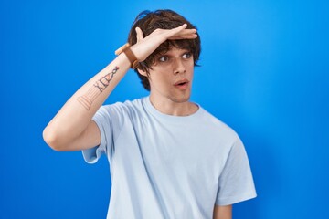 Hispanic young man standing over blue background very happy and smiling looking far away with hand over head. searching concept.