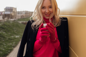 Unrecognizable blond ladylike woman warming with hot cup of coffee, looking at camera on cold...