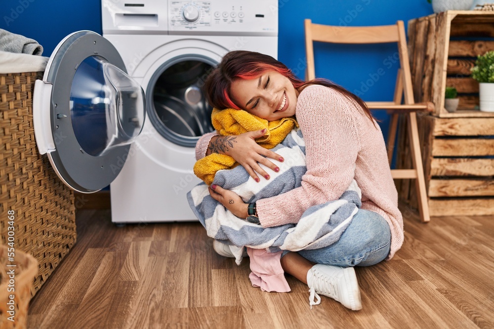 Wall mural Young caucasian woman hugging clothes sitting on floor at laundry room - Wall murals