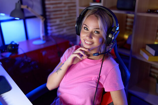Young blonde woman streamer smiling confident sitting on table at gaming room