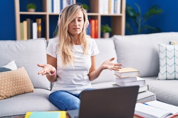 Obraz premium Young blonde woman studying using computer laptop at home clueless and confused with open arms, no idea concept.