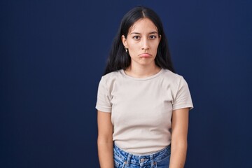 Young hispanic woman standing over blue background depressed and worry for distress, crying angry...