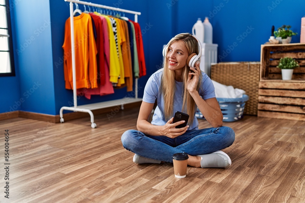 Wall mural Young blonde woman listening to music waiting for washing machine at laundry room - Wall murals