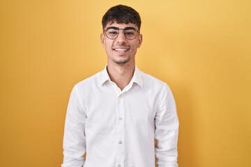 Young hispanic man standing over yellow background with a happy and cool smile on face. lucky person.